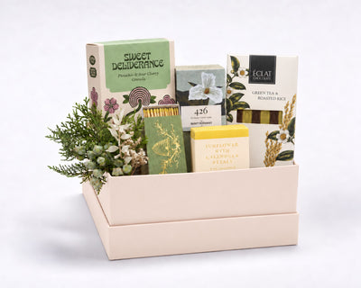 Essential Home Gift Box: The Quiet Botanist 426 mini candle, a green box of matches with a gold bee crest, Saipua sunflower and calendula soap, Sweet Deliverance granola and Éclat green tea and roasted rice chocolate with holiday greenery