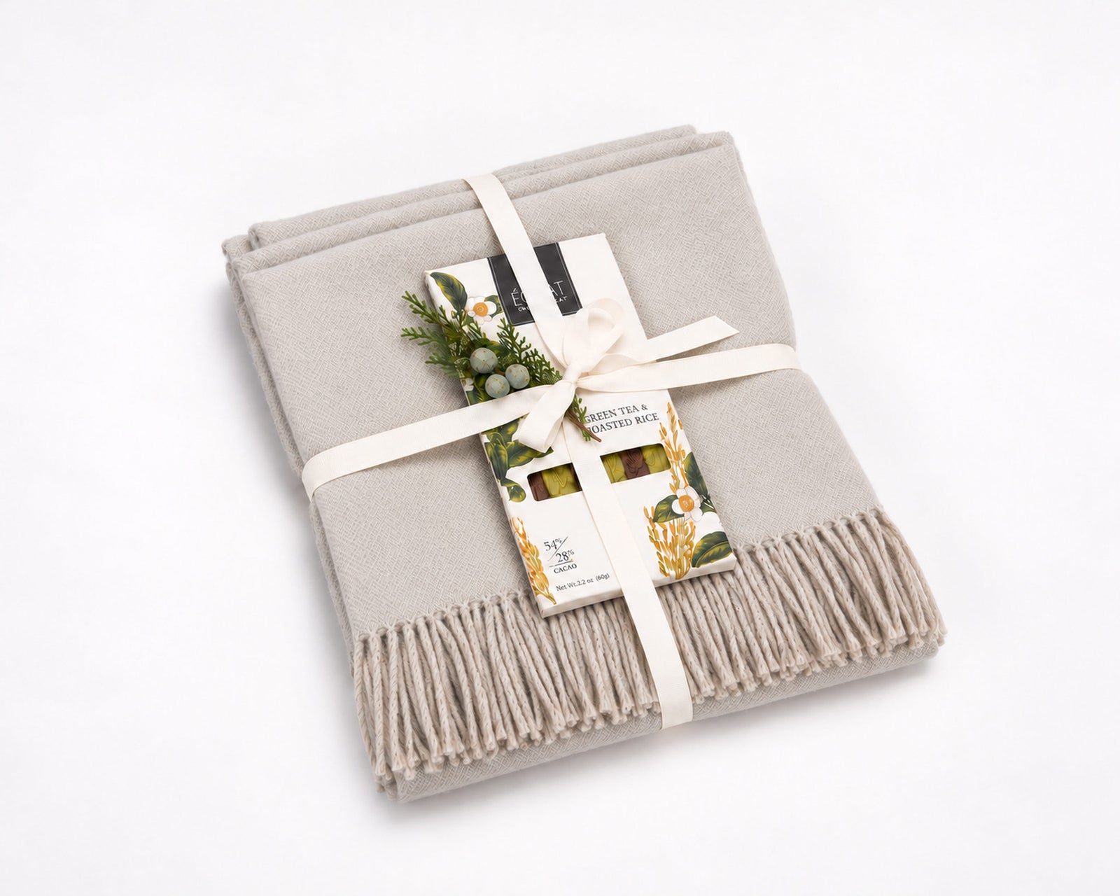 The Cozy Afternoon: a folded London Fog Shupaca baby alpaca throw tied with a cream ribbon, with an Éclat green tea and roasted rice chocolate bar and greenery